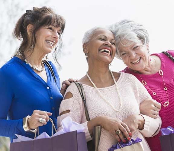 three women holding shopping bags and laughing with each other at Windsor Crossing Senior, Suitland, MD