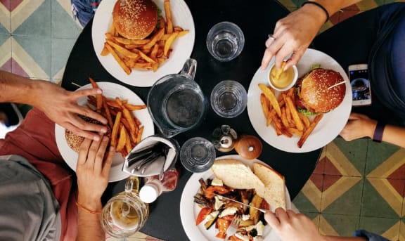 people sitting around a table eating food with burgers and fries