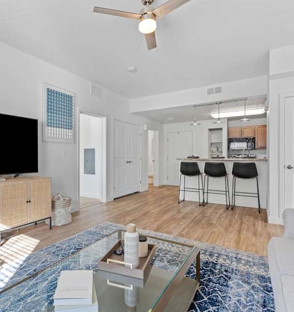 A modern living room with a glass coffee table and a ceiling fan.