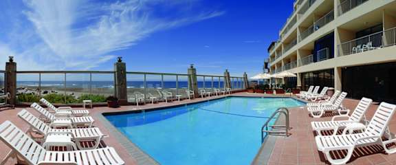 A pool with chairs and a balcony overlooking the ocean.