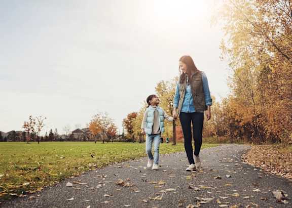 A woman and a child are walking on a path with fallen leaves.