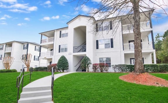 A white apartment building with a tree in front.