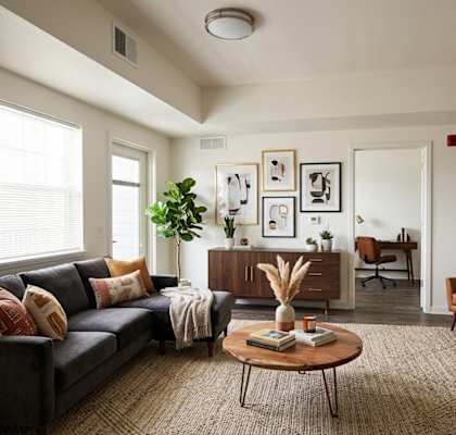 A living room with a grey couch, a brown armchair, a wooden coffee table, and a large window.