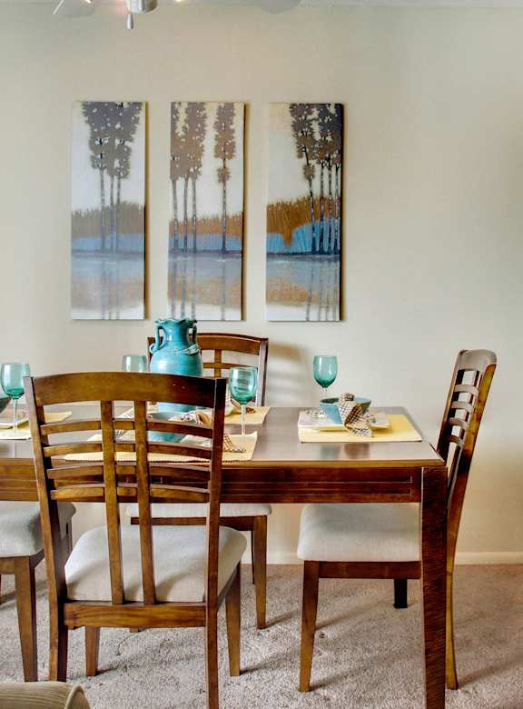 A dining room with a table set for two and a painting on the wall.