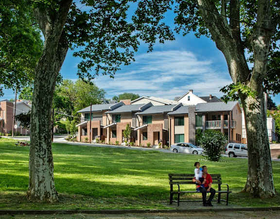 two people sitting on a bench in a park in front of houses