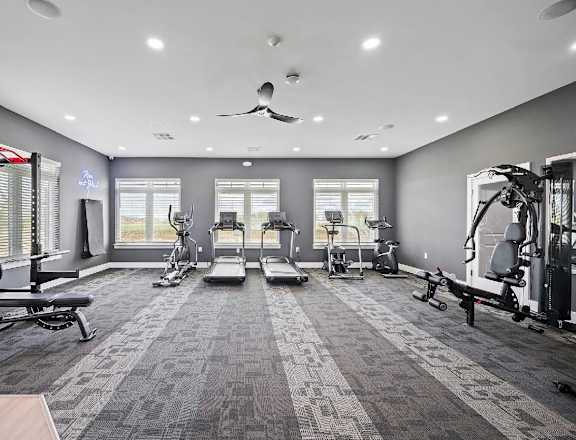 A spacious gym with a variety of equipment and a ceiling fan.