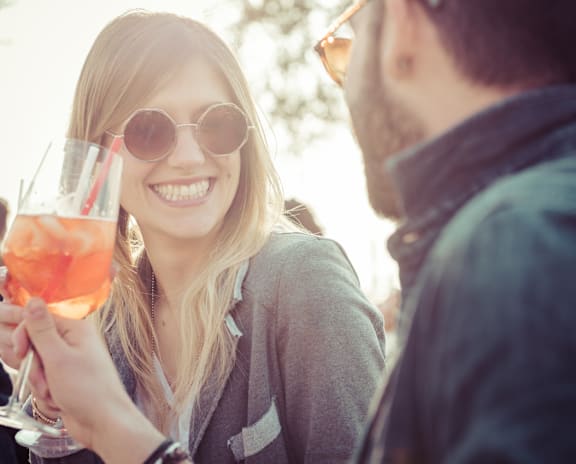 A woman is holding a glass with a drink and smiling while a man looks at her.
