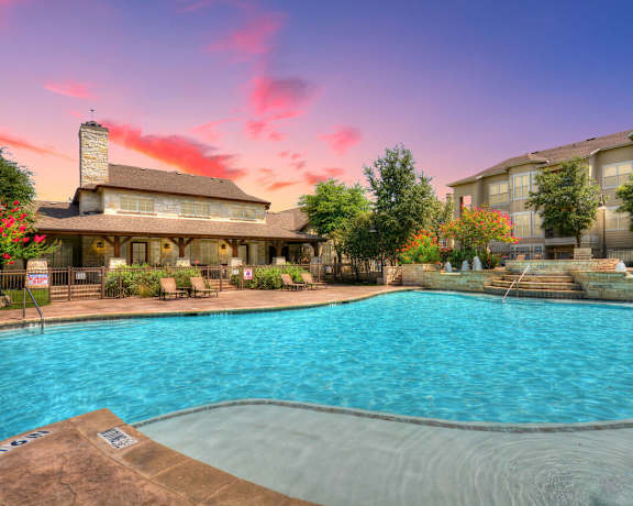 A large swimming pool in front of a building with a sunset in the background.