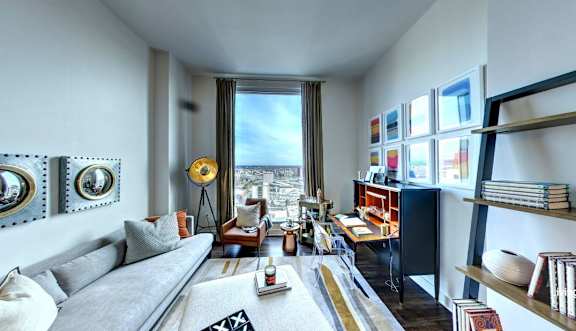 A living room with a grey sofa, a coffee table, and a large window with a view of the city.