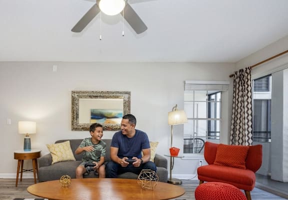 Two men are sitting on a couch in a living room.