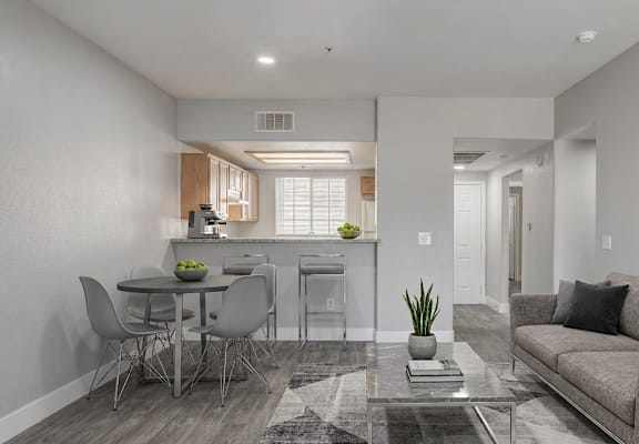 A modern living room with a grey couch, a glass coffee table, and a dining table with chairs.