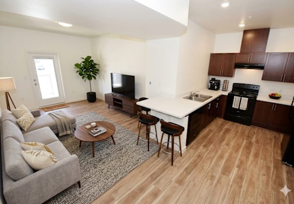 A modern living room with a grey sofa, a wooden coffee table, and a kitchen area in the background.
