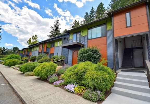 A row of modern townhouses with green bushes in front.