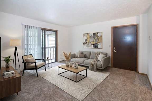 A living room with a grey sofa, a grey armchair, a wooden coffee table, a potted plant, a lamp, and a painting on the wall.