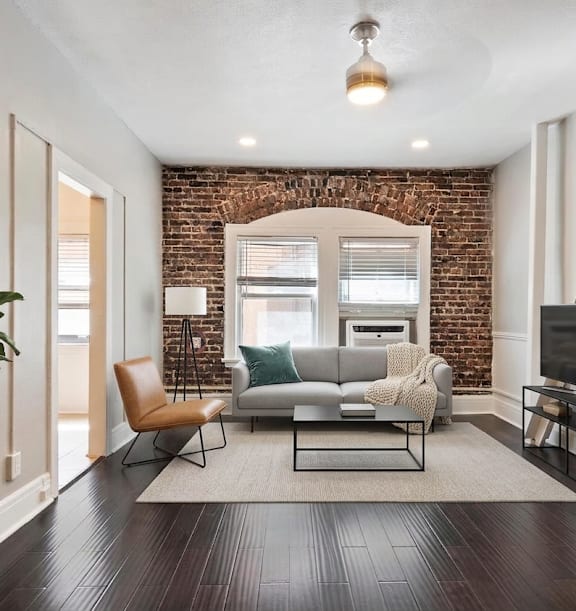 A living room with a brick wall and a grey couch.