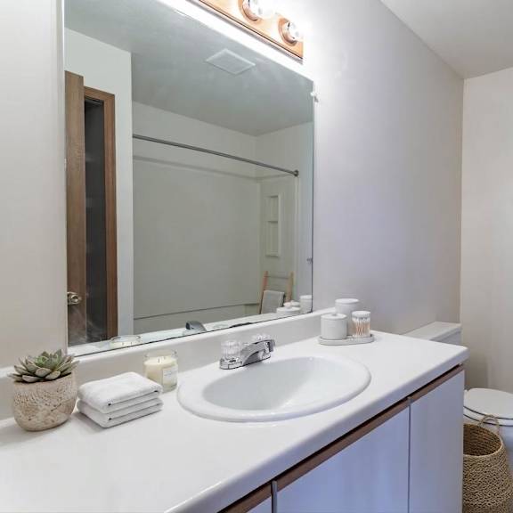 A white bathroom with a sink, mirror, toilet, and a towel rack.