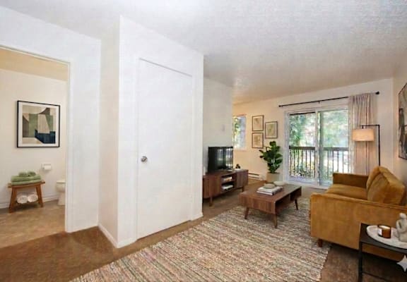 A living room with a couch, a coffee table, a television, and a window with a view of the outside.
