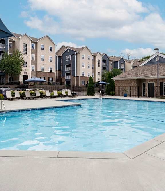 A large outdoor swimming pool surrounded by lounge chairs and buildings.