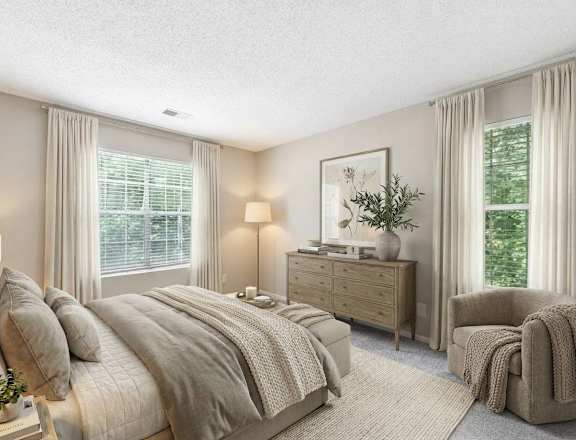 A well-lit bedroom with a large bed, a chair, and a nightstand with a plant on it.
