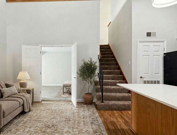 A living room with a couch, a rug, a staircase, and a doorway leading to a balcony.