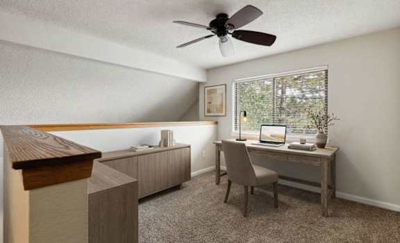 A room with a desk, chair, and a fan.