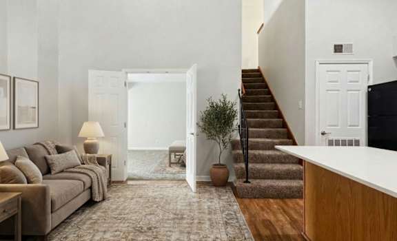 A living room with a couch, a rug, a staircase, and a doorway leading to a balcony.