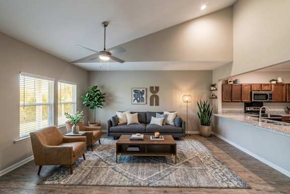 A living room with a grey couch, a brown chair, a coffee table, and a ceiling fan.