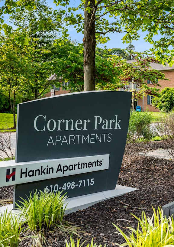 A sign for Corner Park Apartments sits in front of a green lawn.