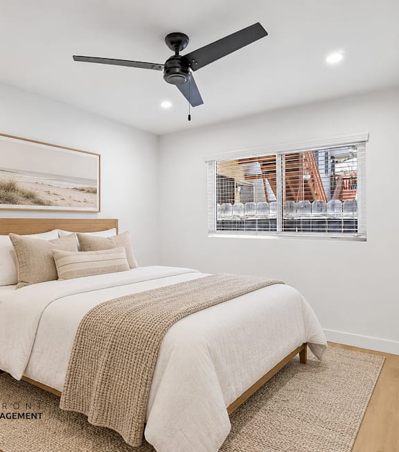 A bedroom with a bed, a ceiling fan, and a window with blinds.