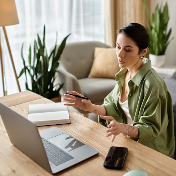A woman in a green shirt is working on a laptop at a wooden desk.