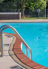 A pool with a metal railing and a brick border.