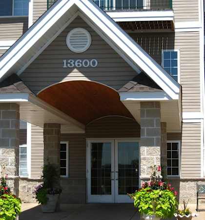 The front of apartment building number 13600 is shown with a bench and flower pots.