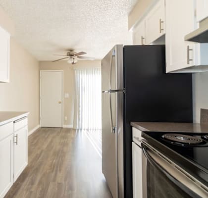 A black refrigerator stands in a kitchen with white cabinets and a sink.
