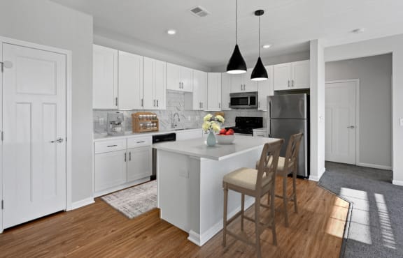 a kitchen with white cabinets and a white island with chairs at Monmouth Row Apartments, Newport, KY