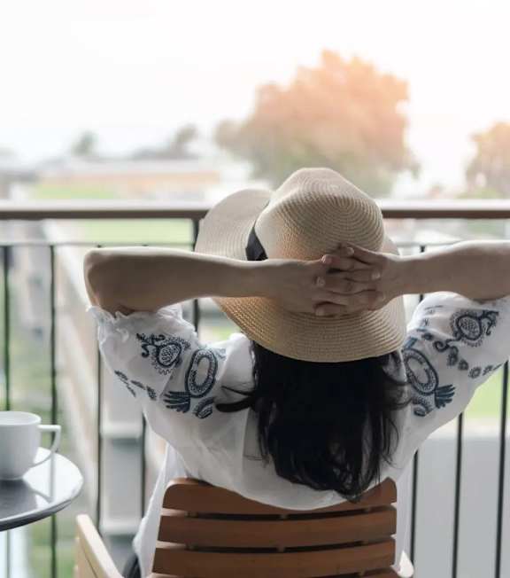 A woman in a hat is sitting on a chair with her back to the camera, looking out of a balcony.at Sylk Towers, Kitchener