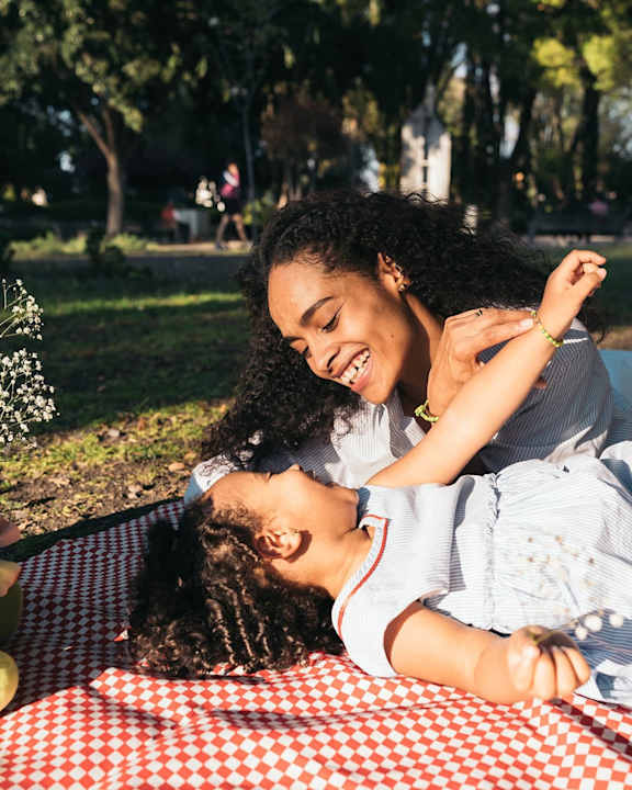 A woman and a child are lying on a checkered picnic blanket in a park at Fernlow Apartments, Houghton Regis LU5 5GX