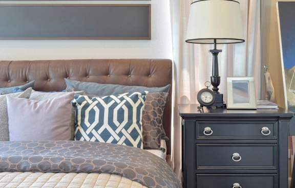 A bed with a brown headboard and a nightstand with a lamp on it.