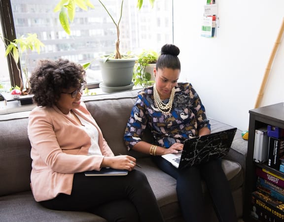 two women sitting on a couch looking at a laptop computer