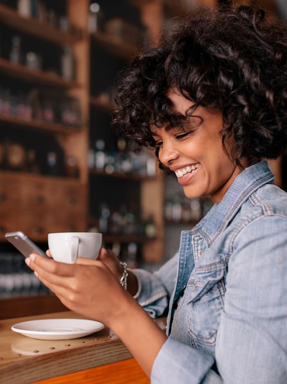 A woman with curly hair is smiling while looking at her phone.