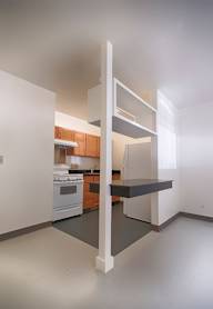 A kitchen with a white wall and a white floor with a white oven and a white fridge.