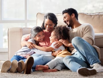 a family of four sits on the floor in front of a couch