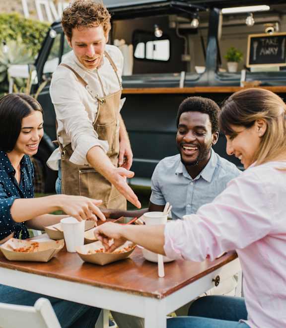 A group of people are gathered around a table, with a person serving food to another person.