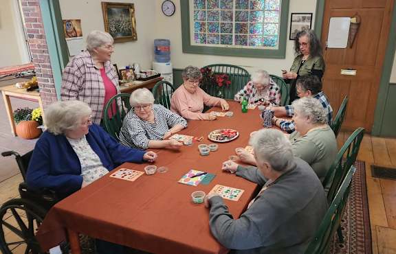 A group of elderly people playing a card game in a room with a stained glass window.