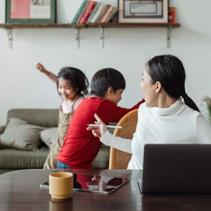 a woman sitting at a table with two children in front of a laptop