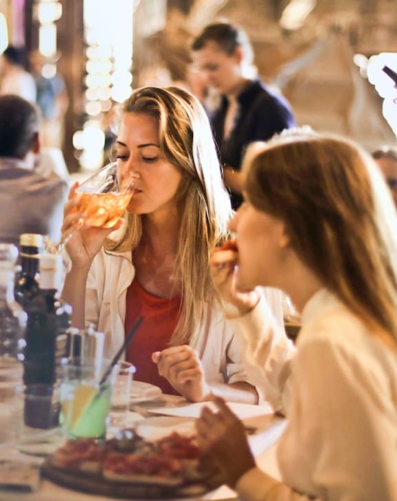 two women sitting at a table in a restaurant drinking wine and eating food