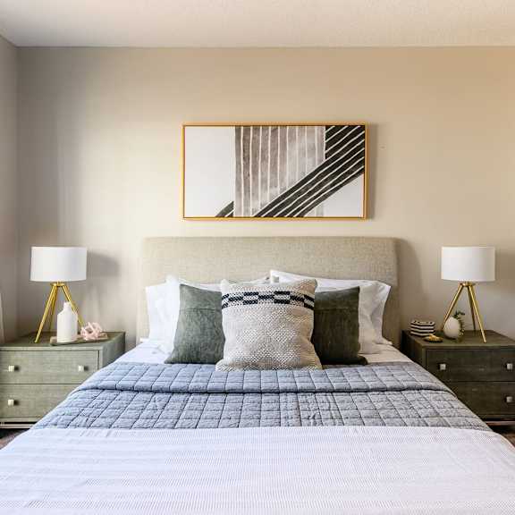 A bedroom with a bed and two nightstands with lamps and a mirror at Retreat at McAlpine Creek Apartments. 