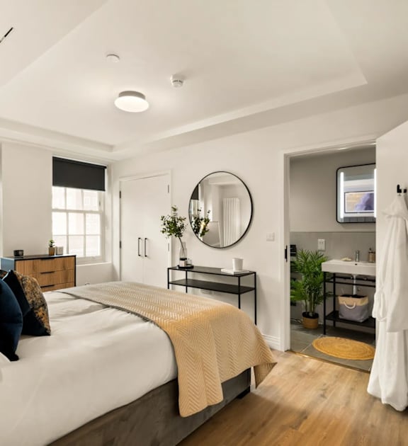 A bedroom with a bed, a mirror, a dresser, and a sink.