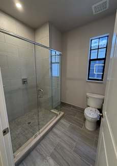 A bathroom with a toilet, a walk-in shower, and a window.