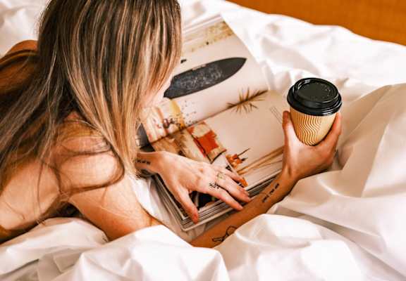 A woman is reading a book in bed with a cup of coffee.at 810 Ashland, Santa Monica, CA