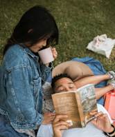 A person is reading a book while another person is drinking from a cup.
